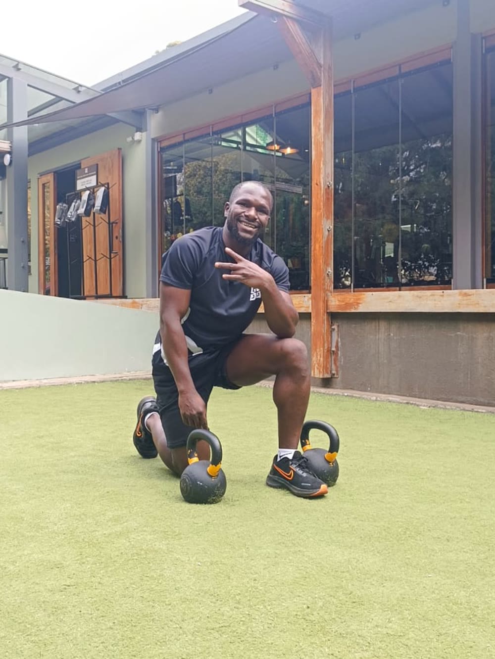 Tim kneeling on the grass between two kettlebells, grinning at the camera
